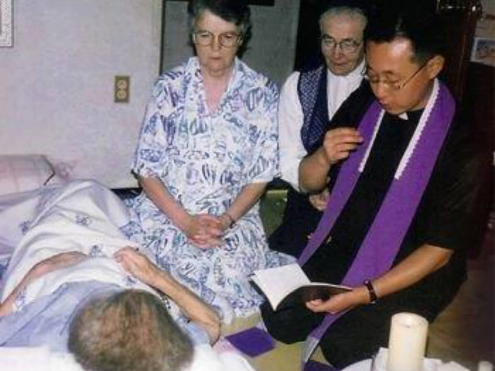 Sr. Taaffe and priest bending over elderly