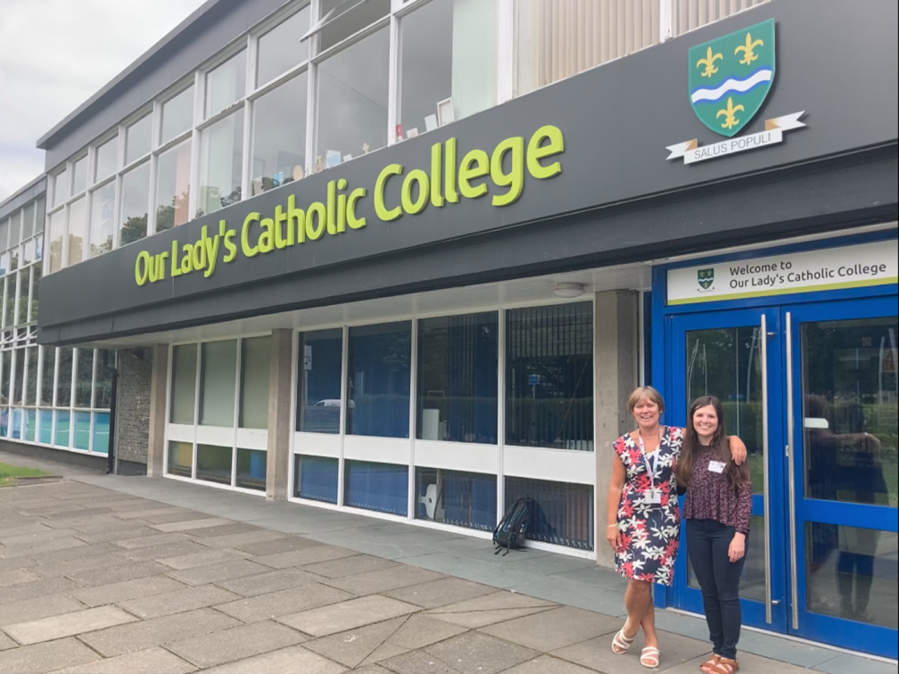 Emma and teacher outside school with school name and logo above them