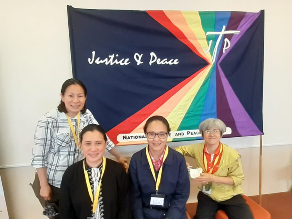 four woemn in front of a colourful 'Justice and Peace' banner