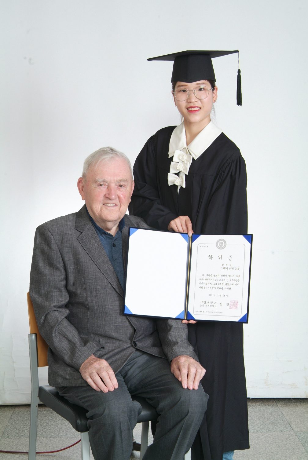 Fr.Noel and Kim in her graduation gown and holding her certificate