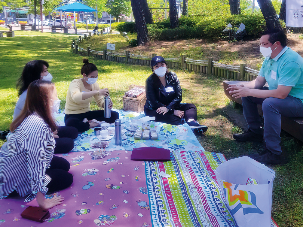 women and priest gather around on an outdoor mat to chat