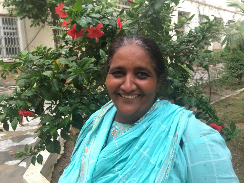 woman in blue stands in front of a flowering red bush