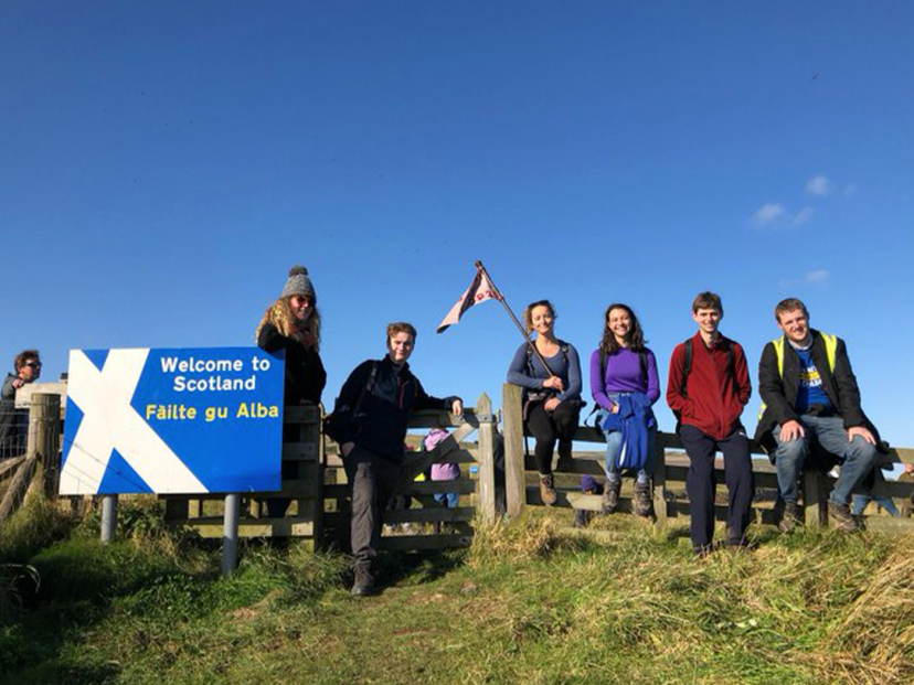 group of young people sit on a fence with blue sky behind them