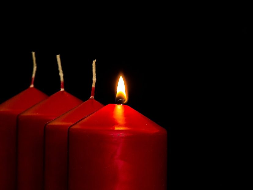 four red candles, one is lit