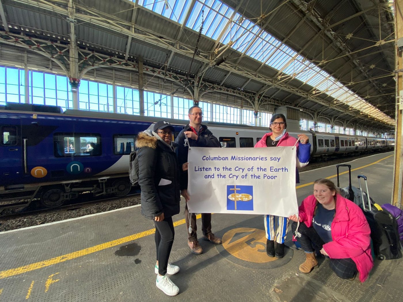 people stand with banner in frnt of a train at a train station