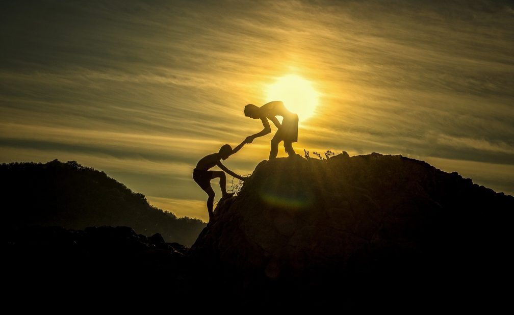 helping someone up a mountain at sunset
