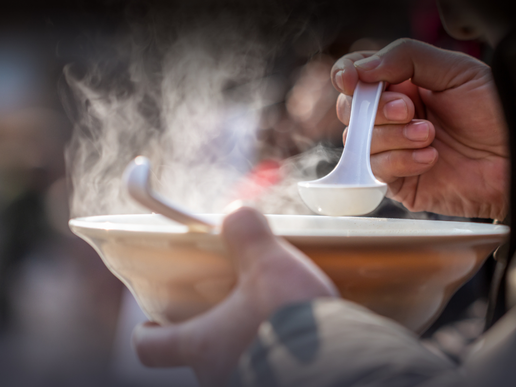 Hands hold a bowl of steaming soup