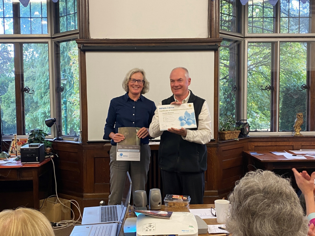Fr. John Boles receives the plaque from Felicite Dodd, welcoming them as a 'Partner in Action'